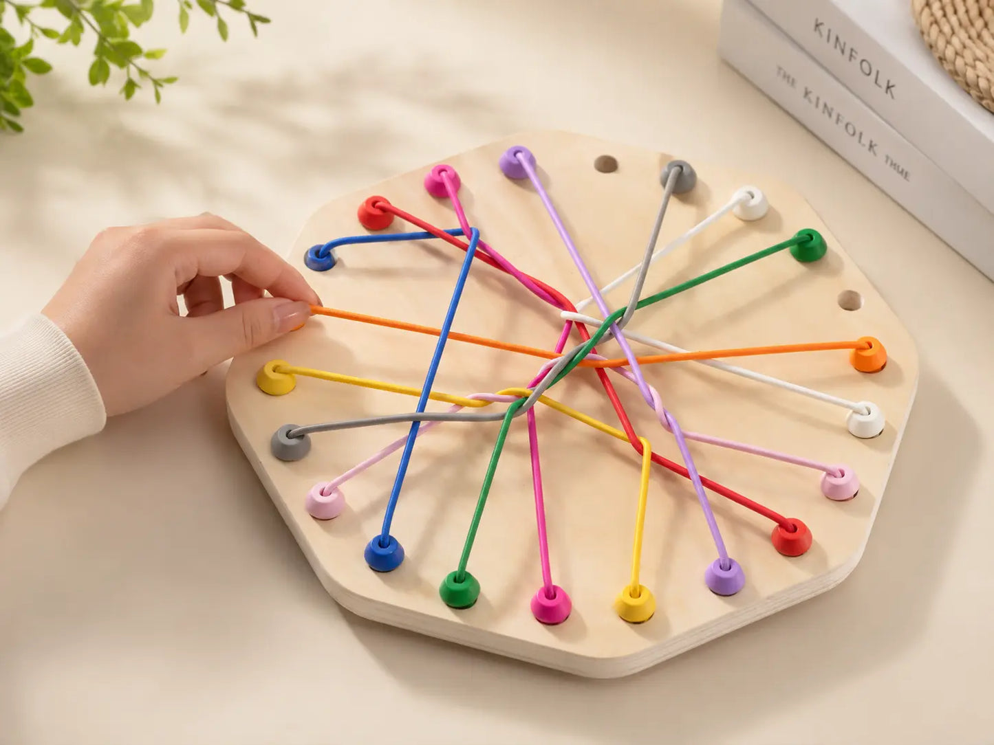 Teenager’s hand lifting an orange cord on a wooden hexagonal rope puzzle designed to support fine motor skills, coordination and problem-solving.
