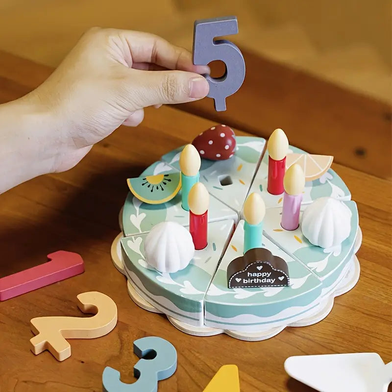Wooden birthday cake toy with candles and a hand placing a number '5' on top, on a wooden surface.